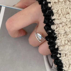 Detailed close-up of a minimalist silver wavy open ring worn on a finger with knitwear