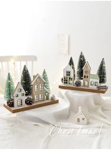 Close-up of lighted wooden Christmas house set with pine cones on white fabric