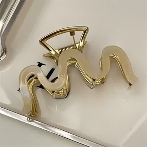Detailed close-up of a wavy cream acetate and gold metal hair claw clip in a white tray