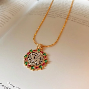 Vintage gold plated portrait coin necklace with colored zircon accents on book background