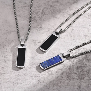 Detailed view of rectangular gemstone pendants with silver box chains on a grey surface