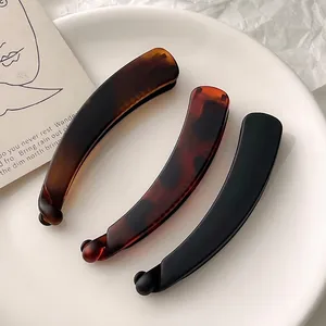 Three matte and tortoise shell banana hair clips arranged on a white decorative plate