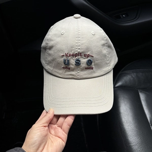 Detail of beige cotton baseball cap with embroidered Keepit up text held by hand