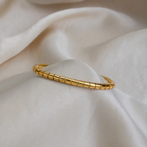 Close-up of golden bamboo joint style stainless steel bracelet on off-white silk fabric