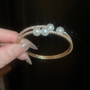 Gros plan sur un bracelet double rang doré orné de perles blanches et diamants pavés