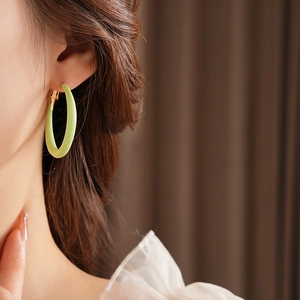 Detail of light green enamel hoop earrings with gold-tone closure on a model