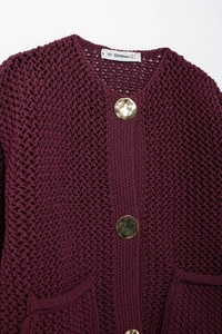 Close-up of chunky burgundy knit cardigan featuring textured weave and large gold disc buttons