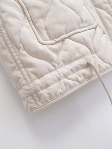 Detail view of the drawstring hem and quilted diamond texture on the cream sleeveless vest