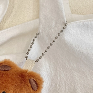 Detail of brown plush bear pendant attached to a white canvas bag with silver bead chain