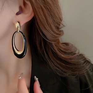 Macro detail of oversized oval enamel earrings in gold and black on a female model
