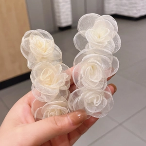 Detailed view of two white mesh camellia hair clips held by hand for delicate hair styling