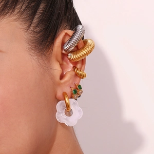 Close-up of stacked gold earrings with white flower charm and green emerald studs