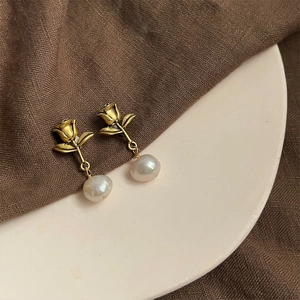 Close-up of golden rose stud earrings with natural baroque pearl drops on ceramic plate