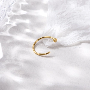 Minimalist gold G23 titanium C-shaped nose ring with flat end on textured background