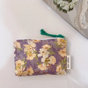 Close-up of floral cotton coin purse with zipper and tassel detail on a white desk