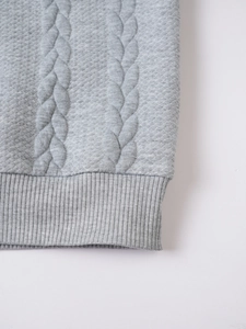 Close-up of grey cable knit texture and ribbed hem on a warm turtleneck sweater