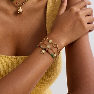 Detail of layered gold stainless steel bracelets with sun charms and colorful gemstones
