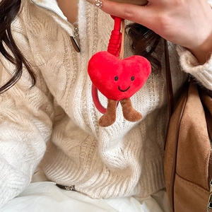 Close-up of a red plush heart charm with an embroidered smiley face on a brown suede bag