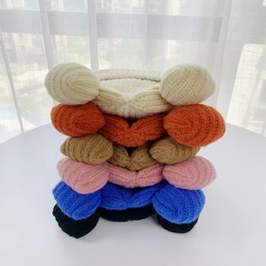 Vertical stack of six colorful knitted beanies with bear ears in soft indoor lighting