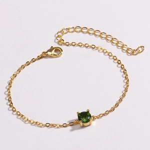 Detailed shot of golden link bracelet with a green round stone and lobster clasp closure