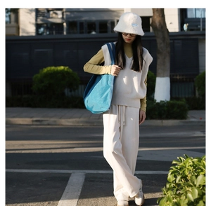 Close-up of stylish blue canvas shoulder bag paired with cream knit vest and bucket hat