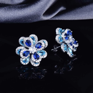 Detailed close-up of blue zircon flower earrings with silver studs on grey silk