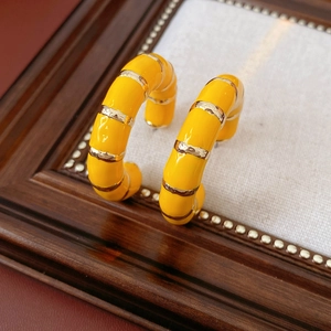 Macro detail of vintage yellow enamel C-shaped earrings with gold stripe accents