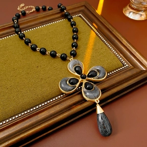 Vintage gold cross necklace with black stones and water drop pendant on a wooden frame