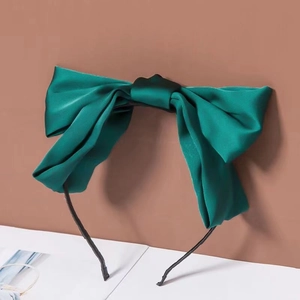 Macro detail of the dark green satin bow hair clip on a black headband base