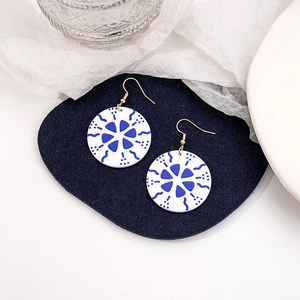 Macro detail of round blue and white porcelain pattern drop earrings on blue felt