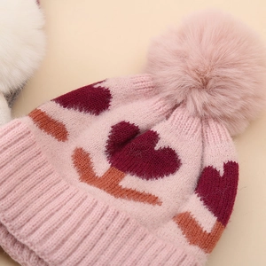 Pink winter knit baby hat with heart pattern and large faux fur pompom for newborns