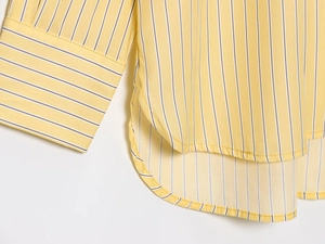 Dettaglio del polsino della camicia a righe gialle e dell'orlo laterale curvo in cotone