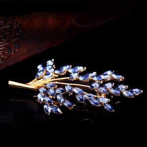Detail shot of golden leaf brooch with blue marquise crystals on a black reflective surface