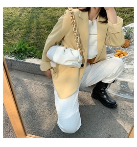 Close-up of white pleated cloud bag with chunky gold chain strap on a stylish outfit
