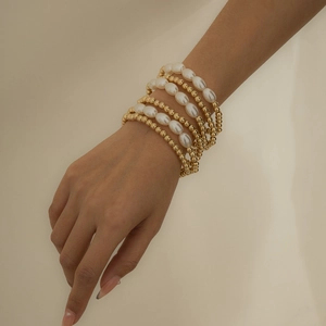 Minimalist gold beaded bracelets layered with elegant imitation pearls on a woman's wrist
