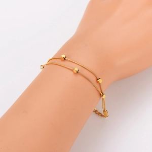 Double-layered gold snake chain bracelet with metallic beads on a model's wrist