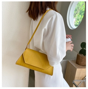 Detail shot of yellow baguette bag showing crocodile skin texture and slanted flap design