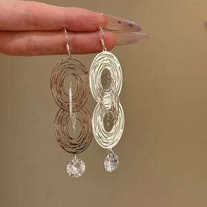 Close-up of silver hollow oval earrings with sparkling zircon pendant details