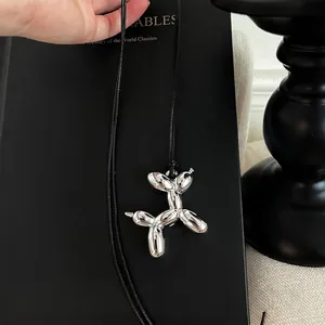 Silver mirror balloon dog pendant on black slim cord leaning against a black book