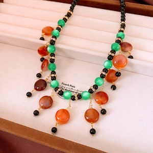 Detail of vintage beaded necklace with green cat-eye and orange agate beads on velvet