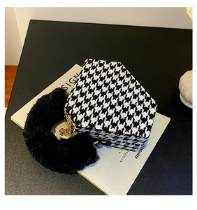 Macro view of houndstooth handbag featuring black plush handle and gold chain detail