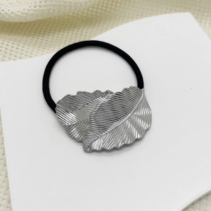 Close-up of silver metal leaf charm with detailed veins on black elastic hair tie