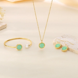 Detail view of gold jewelry set with green opal and pearl on beige silk background