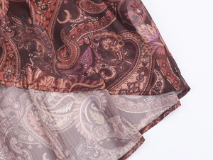 Detail of bohemian chiffon dress featuring reddish-brown paisley print and hem stitching