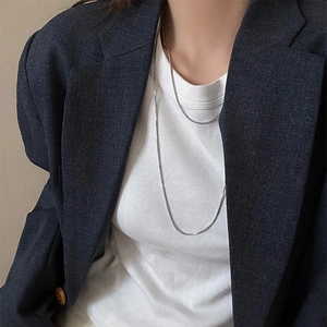 Close-up of sleek silver snake chain necklace styled with a grey blazer and white top