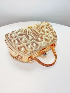 Detailed view of golden rhinestone evening bag with pearl peacock pattern and metal handle