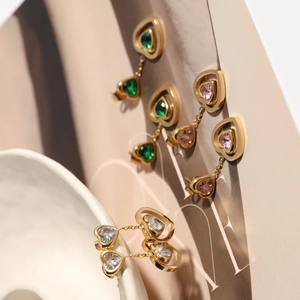 Elegant gold heart tassel earrings with emerald and pink stones in a minimalist setup