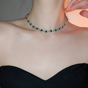 Close-up of a silver flower necklace with green gemstones worn on a model's neck
