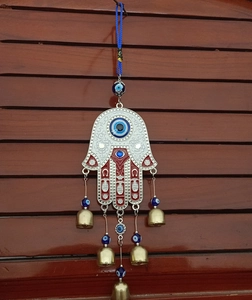 Hamsa Hand evil eye wall hanging with five brass bells against wooden shutter background