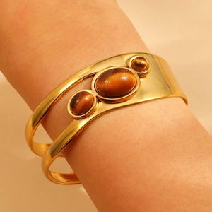 Detail of gold-plated open bangle featuring three oval cat-eye stones in a vintage style